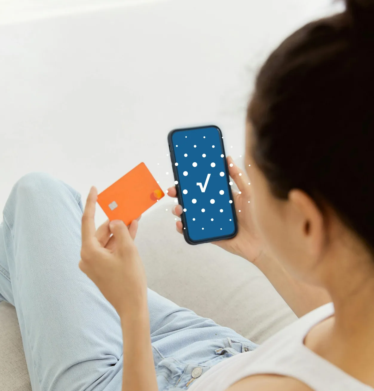 una mujer con su celular y su tarjeta de crédito en mano, la pantalla de su celular muestra un icono de aprobado